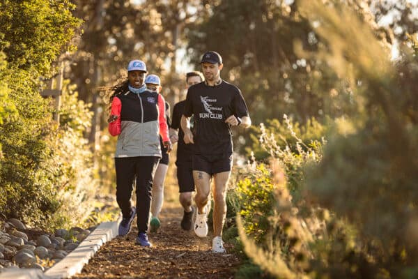 Group of runners jogging along a tree-lined trail at golden hour during a Treasure Island community run club event.