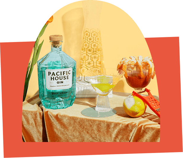 Pacific House Gin Deep Umami bottle styled with a green gin cocktail, citrus garnish, and bar tools on a textured table, showcasing premium coastal botanical craft spirits.