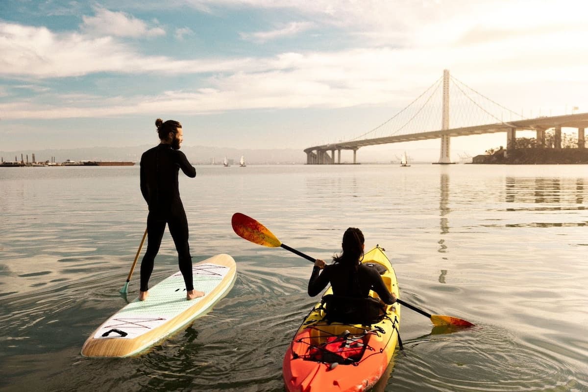 Kayaker and paddleboarder on calm San Francisco Bay waters near Treasure Island with the Bay Bridge at sunrise.