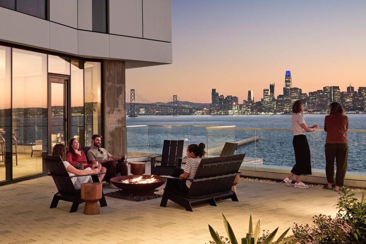 Residents relaxing on a waterfront terrace with fire pit seating and panoramic views of the San Francisco Bay and skyline at sunset.