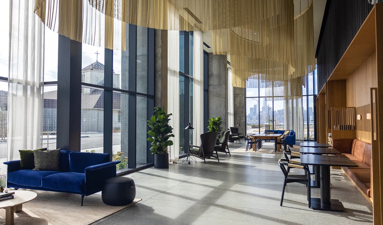 Sunlit lobby lounge at a Treasure Island residential community with floor-to-ceiling windows and views of the San Francisco skyline.