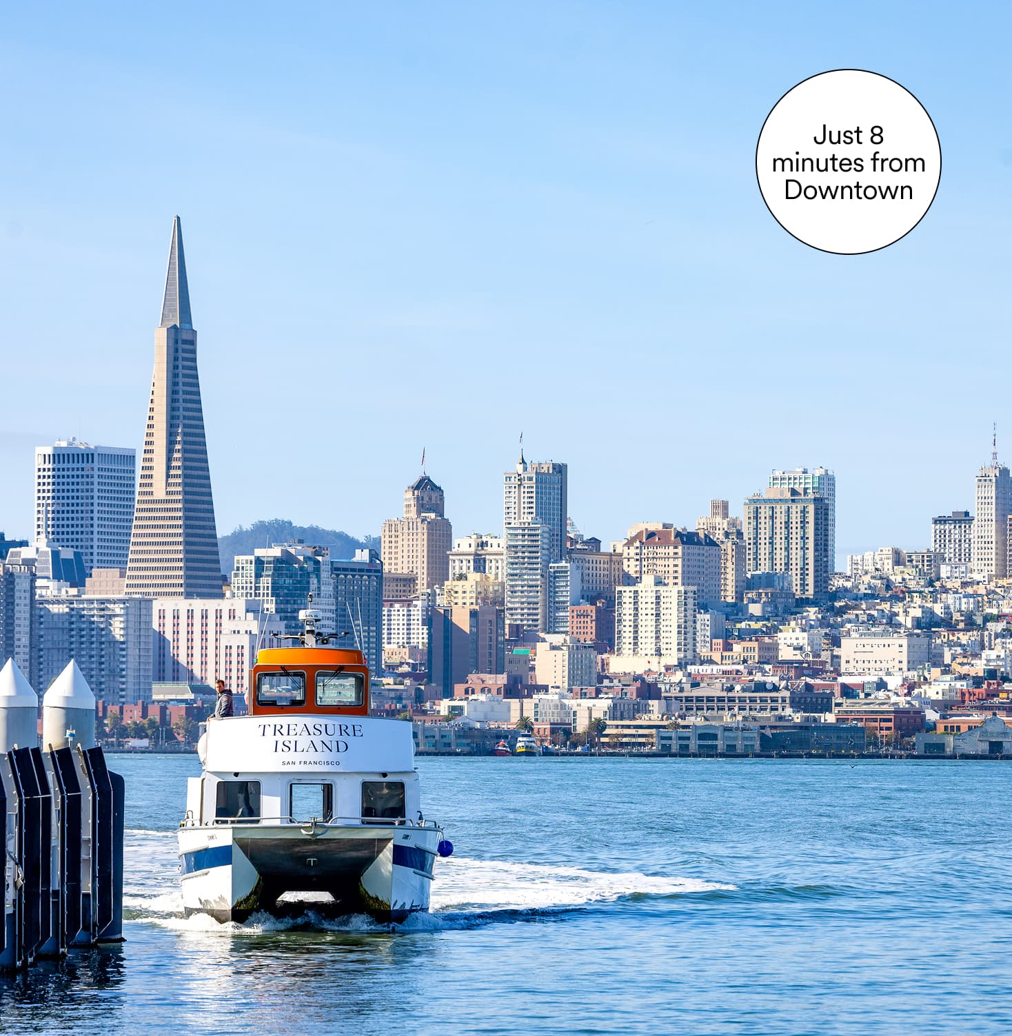 A ferry labeled “Treasure Island – San Francisco” heads across the bay toward the city skyline, with the Transamerica Pyramid and surrounding high-rises visible under a clear blue sky. A note in the corner reads, “Just 8 minutes from Downtown.”