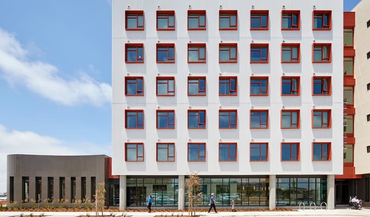Six-story residential apartment building at Maceo May on Treasure Island, with a modern façade, large windows, and landscaped walkways and greenery in the foreground.