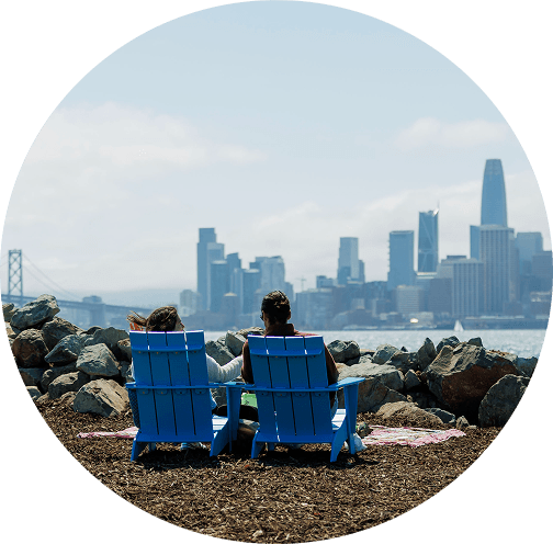 Couple sitting in blue Adirondack chairs by the waterfront overlooking the San Francisco skyline and Bay Bridge