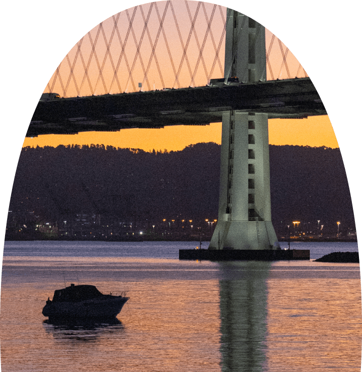 Bay Bridge support tower at dusk with a small boat on calm water in the foreground