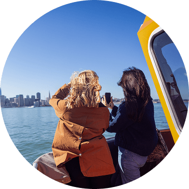 Two people on a boat taking a photo with a city skyline across the water