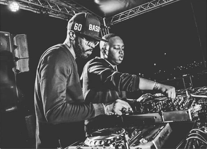 Two DJs performing live on stage, adjusting mixing equipment under concert lighting