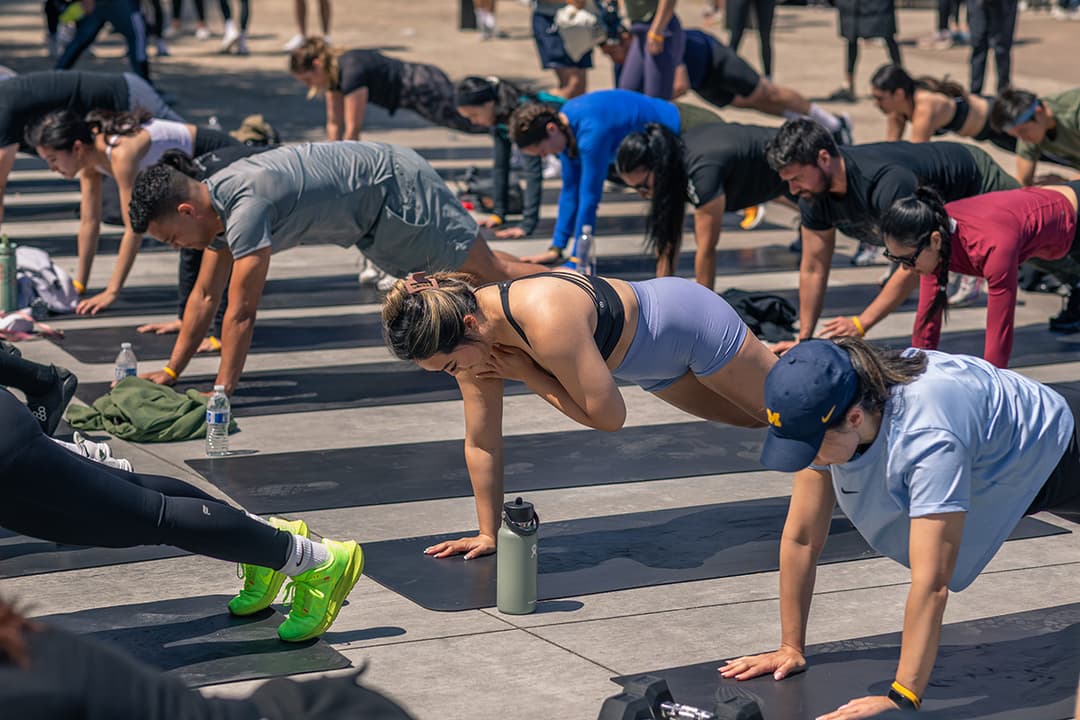Group fitness class exercising on mats outdoors, with participants holding plank positions during a waterfront workout.