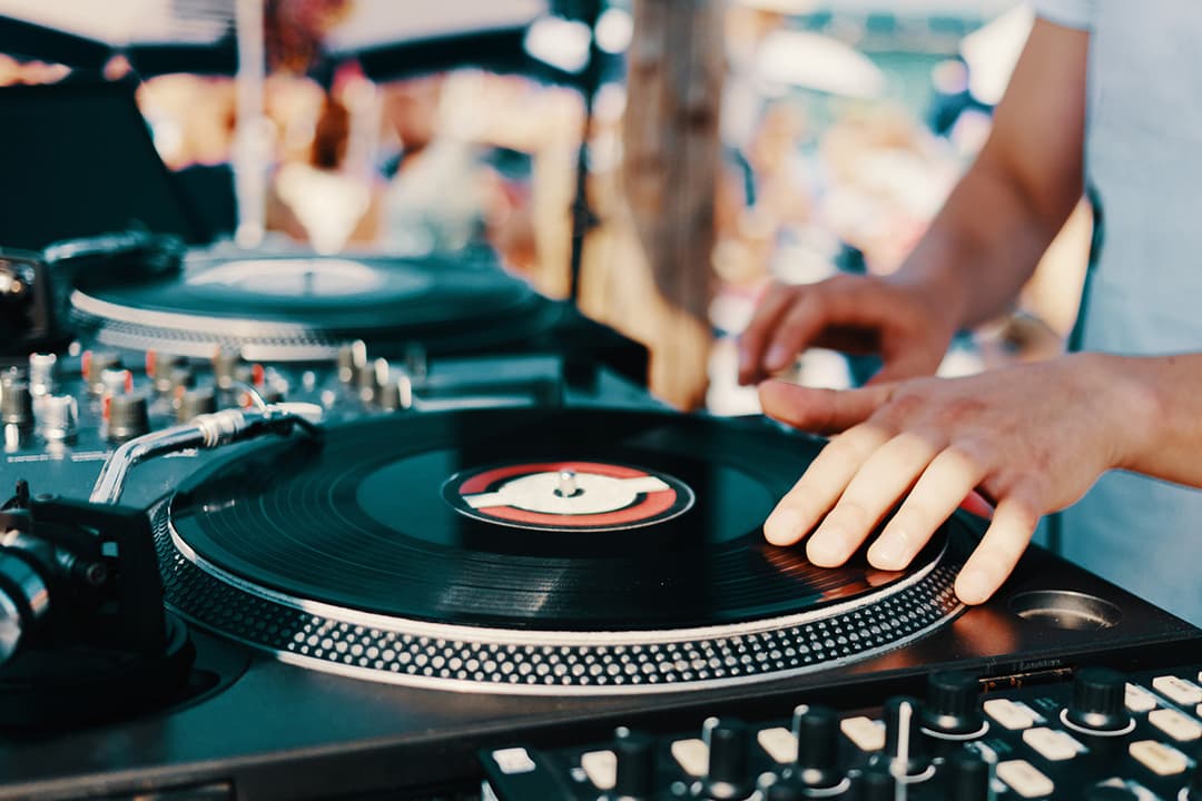 Close-up of a DJ mixing vinyl records on turntables during an outdoor event, representing live music at Gold Bar during sunset.