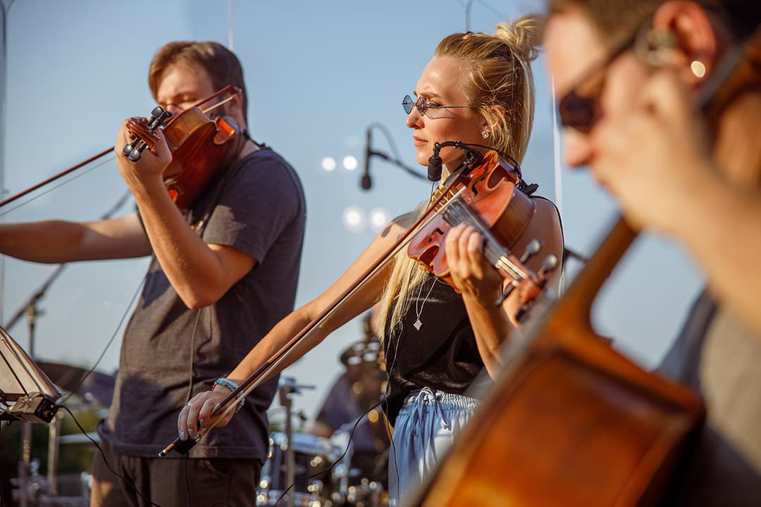 String musicians playing violins during an outdoor live performance with microphones and stage lighting