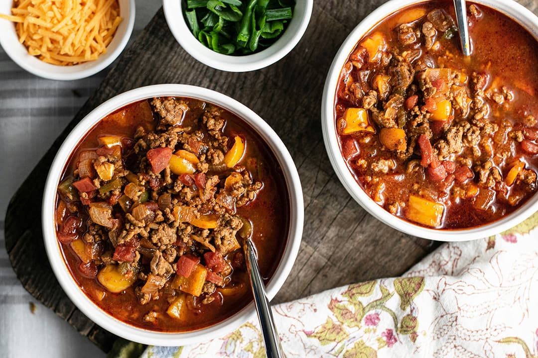 Bowls of chili topped with herbs and spices, ready for a community chili cook-off.